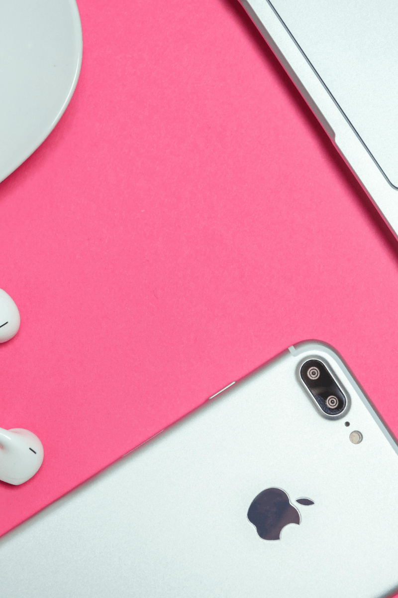 Neon pink table with silver phone, laptop, and headphones on it